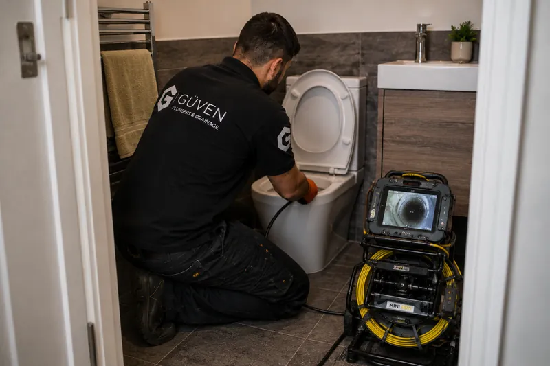 Güven drainage engineer using drain inspection equipment at a toilet